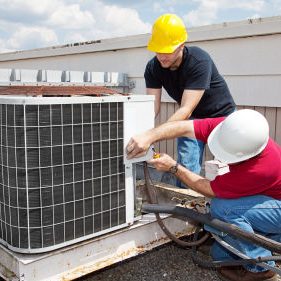 Two workers on the roof of a building working on the air conditioning unit.